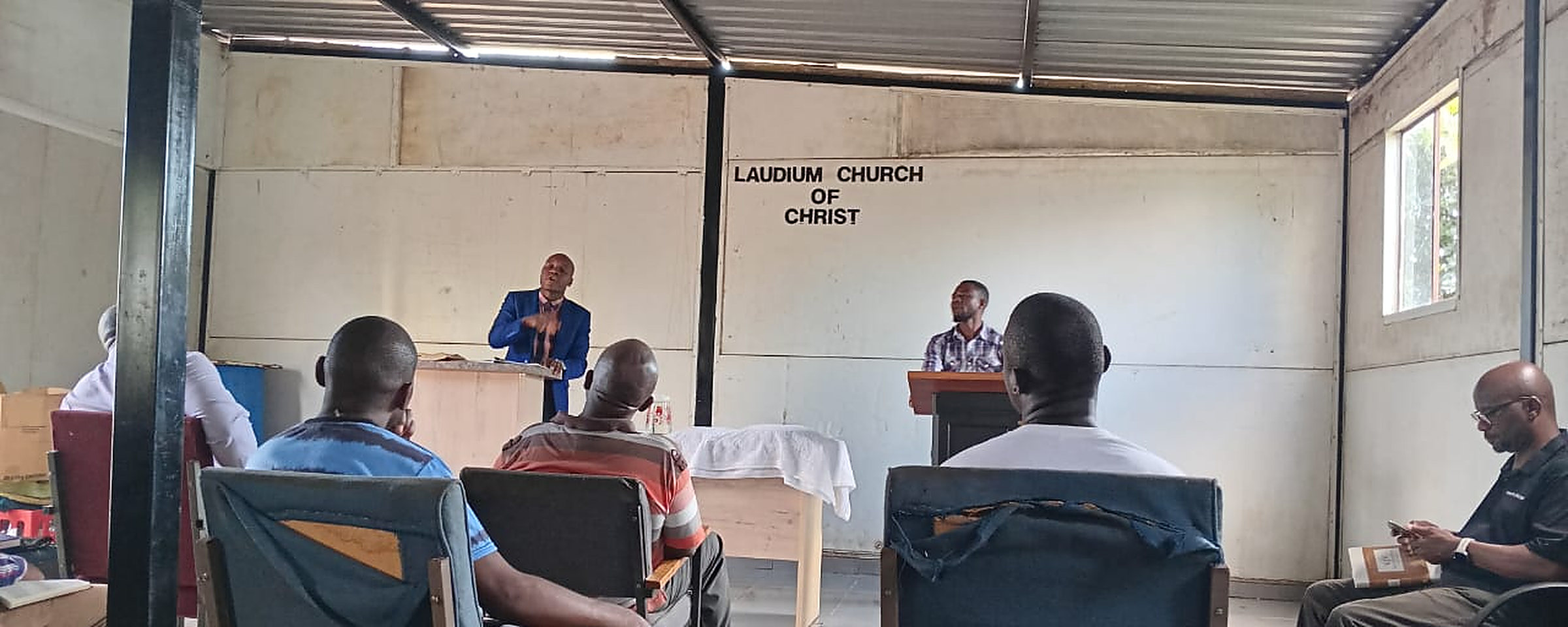 A preacher teaches from a wooden stand at our church of Christ in Laudium while members sit and listen