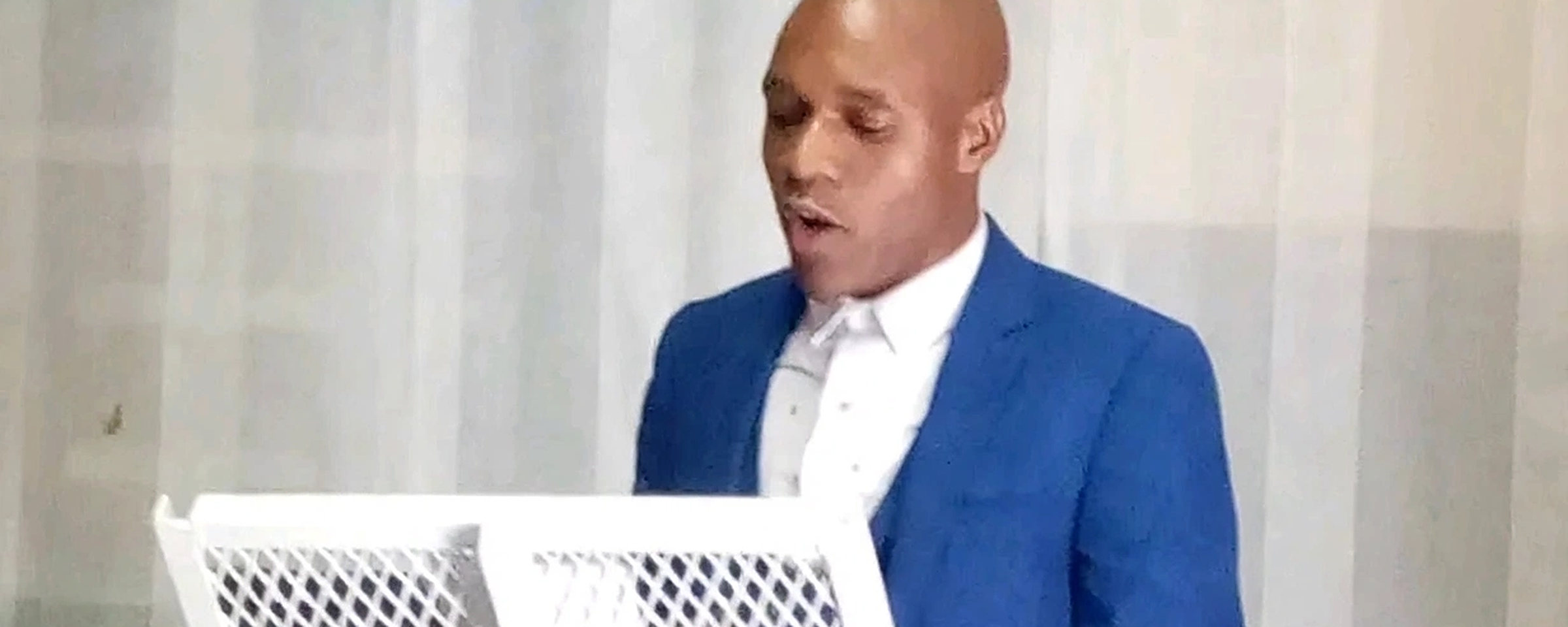 A preacher in a blue suit reads from a white stand during one of our Church of Christ sermons