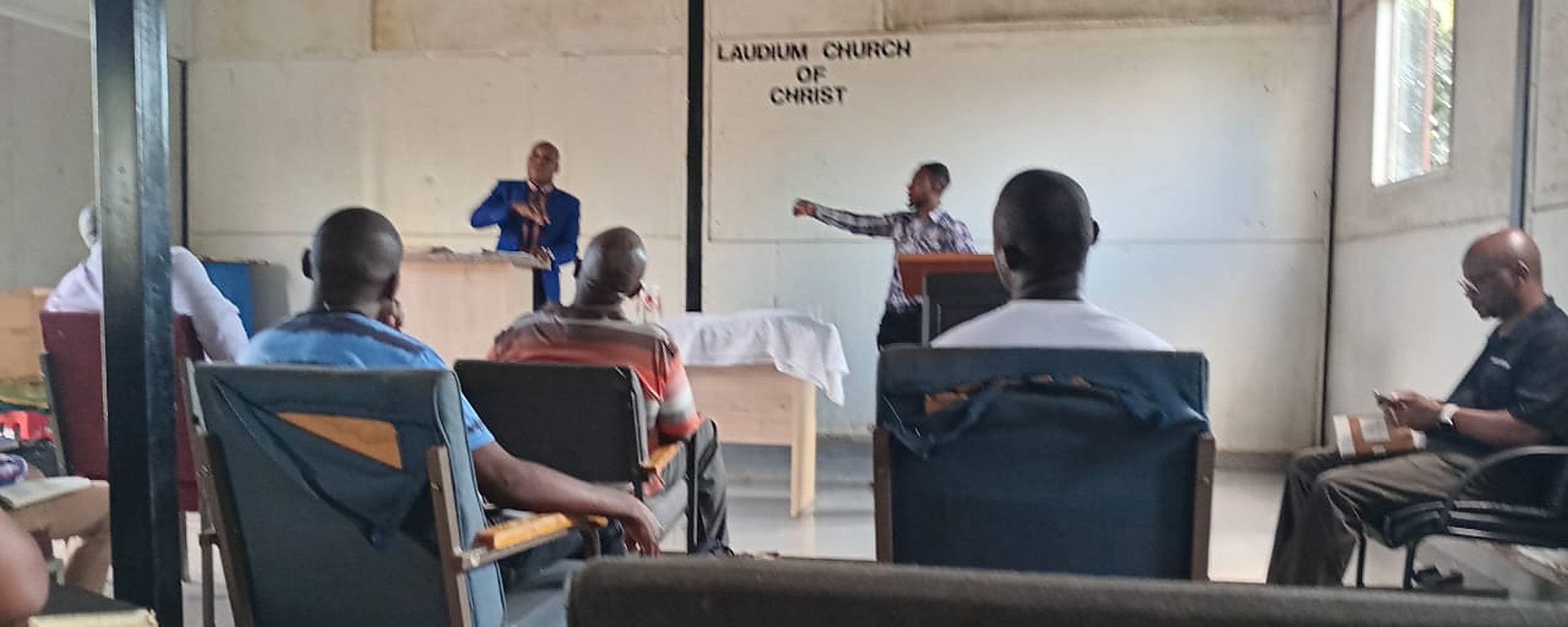 Members sit in chairs and two men speak from stands during our church service times in Pretoria